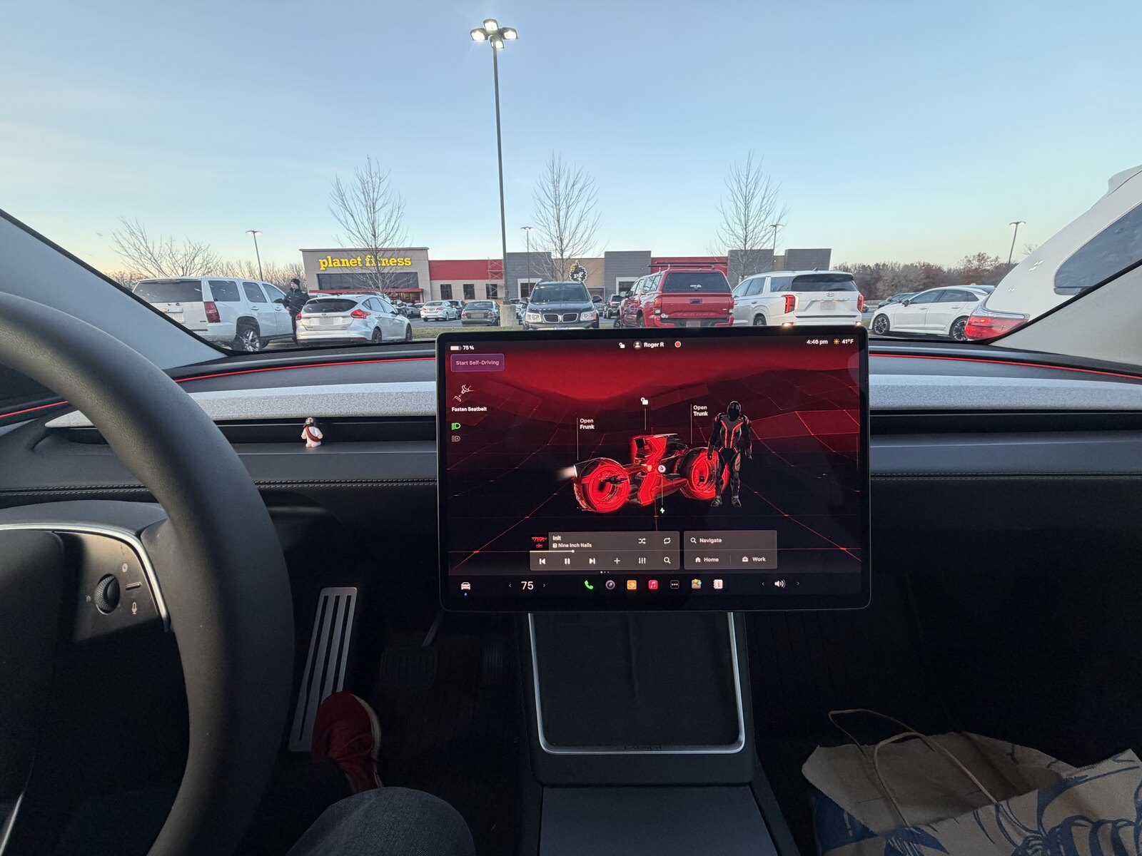 Tesla center screen showing the red TRON: ARES Light Cycle visualization, with a Planet Fitness parking lot beyond the windshield.