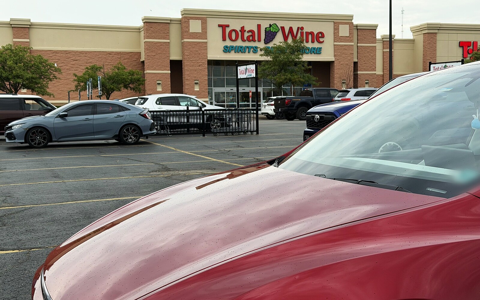Red Tesla Model Y parked alone in an empty row of the Total Wine parking lot, with the store and every other car parked far up by the entrance.